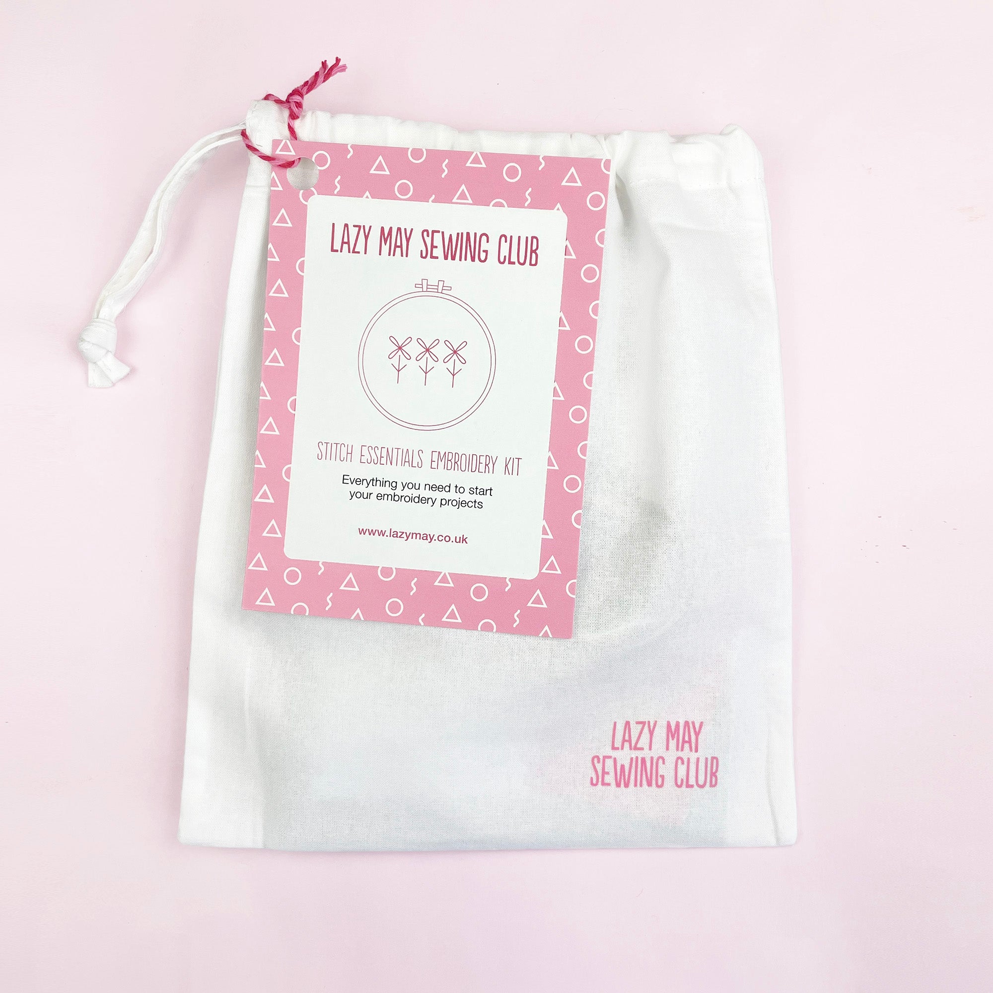 White drawstring bag with a pink tag from Lazy May Sewing Club containing embroidery starter kit materials