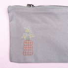 Gray pouch with embroidered flowers on a light pink background