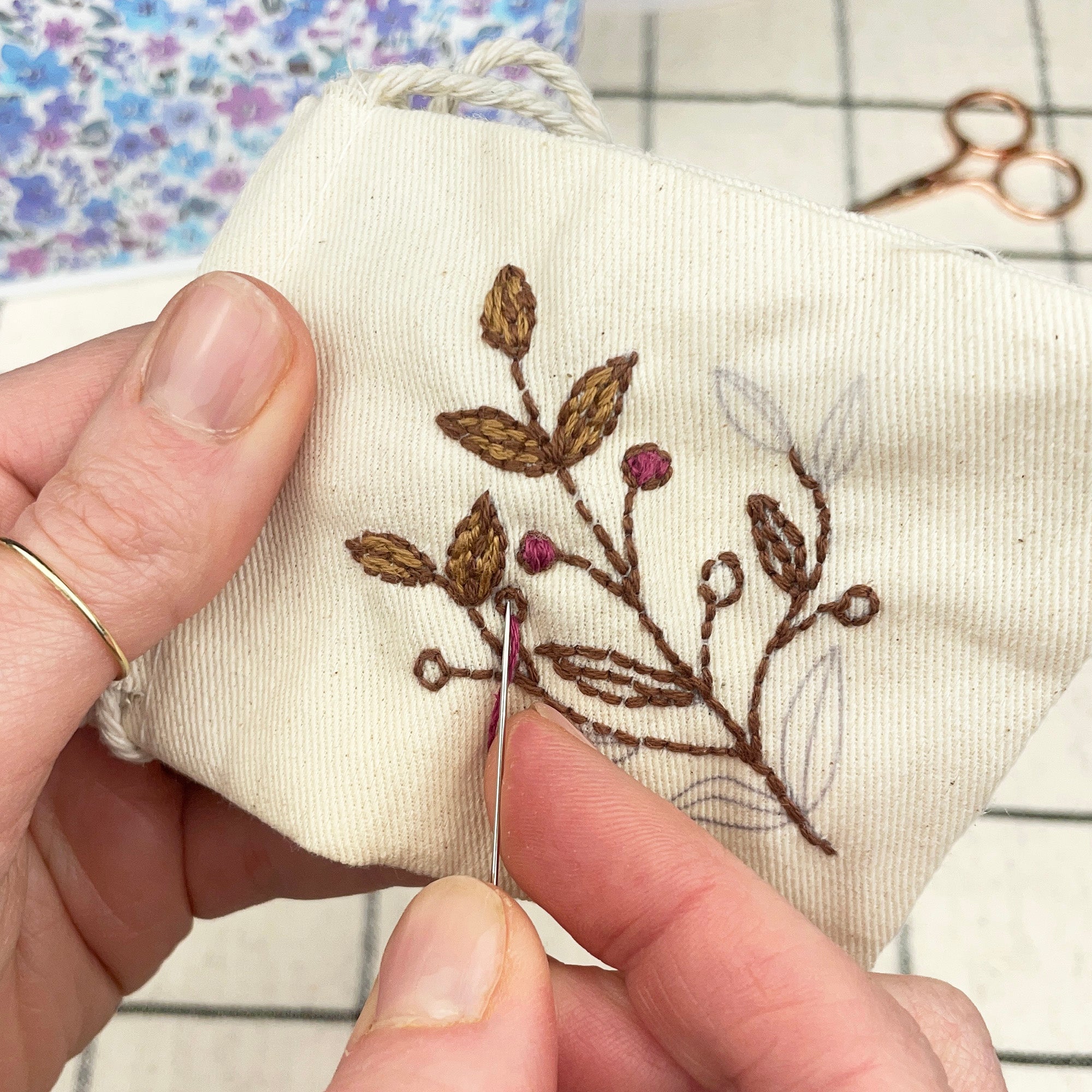 Person embroiderying a floral design on fabric with a needle and thread.