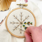 Embroidery hoop with a snowflake design being worked on, with a hand holding a needle.