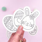 A hand holding Easter embroidery patterns featuring a bunny and decorated Easter eggs. Stick and stitch dissolving embroidery patterns for modern Easter crafts.