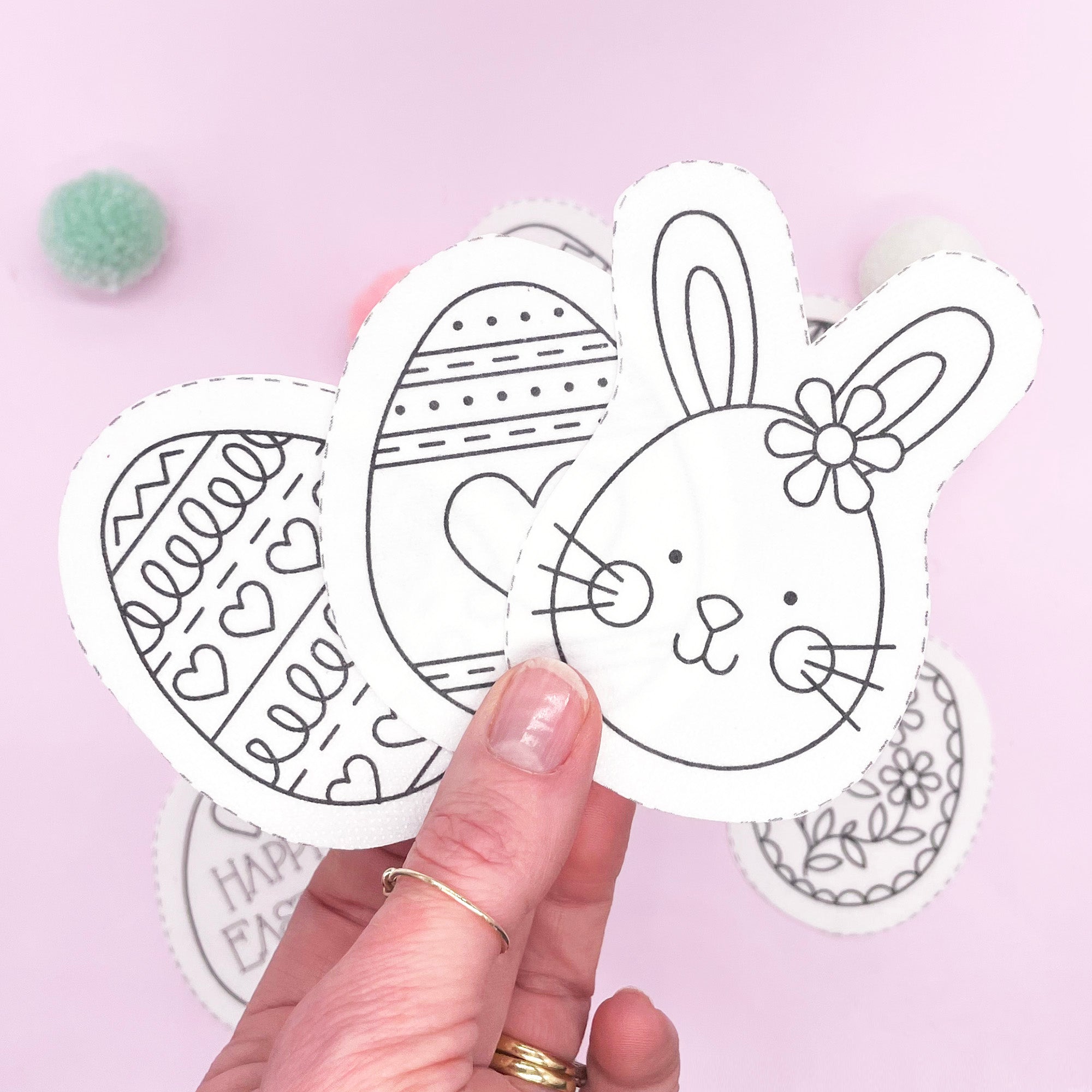 A hand holding Easter embroidery patterns featuring a bunny and decorated Easter eggs. Stick and stitch dissolving embroidery patterns for modern Easter crafts.