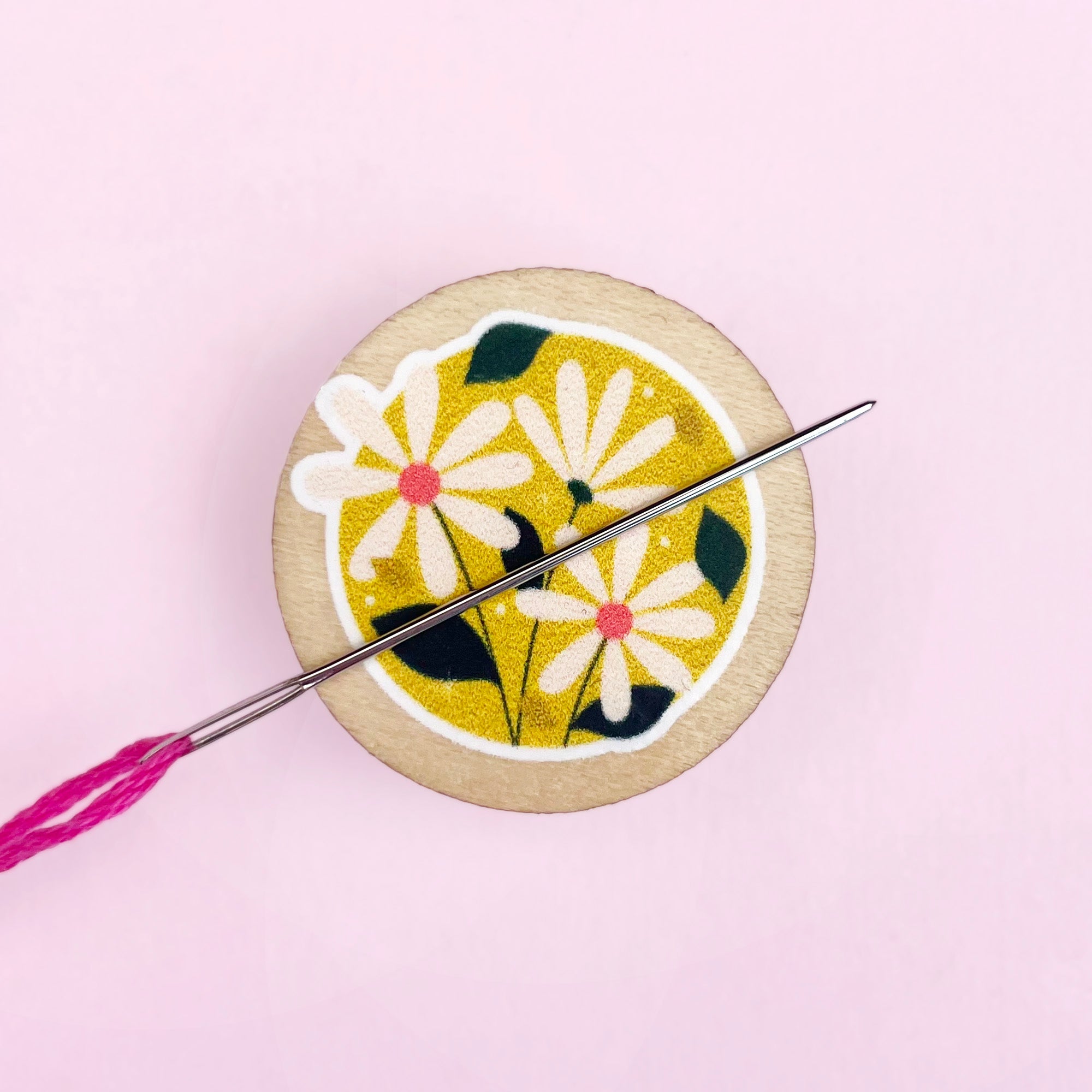 Embroidery needle minder with floral design and needle on a pink background