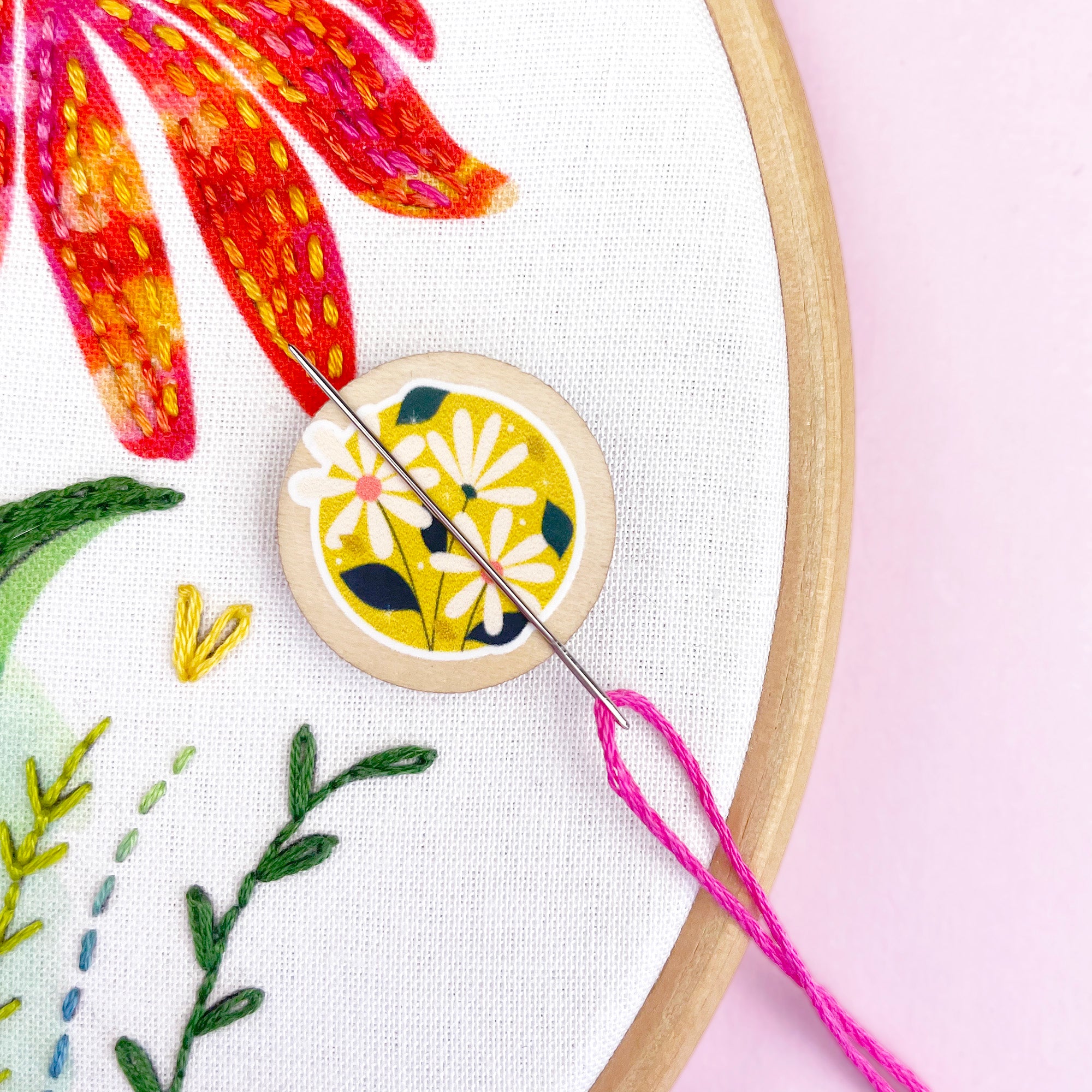 Embroidery hoop with floral embroidery and a magnetic needle minder with a floral design.