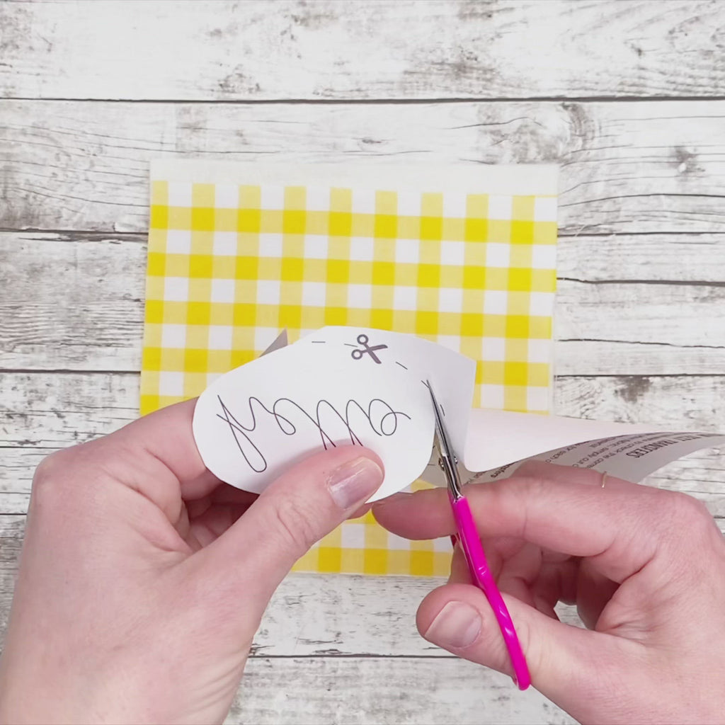 Video showing iron on embroidery pattern of the word hello being ironed onto yellow gingham fabric followed by three flowers being ironed onto white embroidery fabric iron on transfer patterns in action