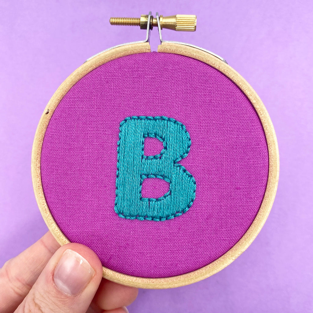 Close-up of purple embroidery hoop stitched with a bright blue letter B from Lazy may embroidery alphabet iron on embroidery patterns
